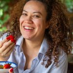 Smiling woman eating strawberries in a cozy restaurant with natural light and a warm lifestyle atmosphere.