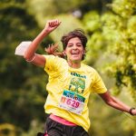 Joyful female runner in yellow participates in an outdoor race amidst lush greenery, embodying athletic enthusiasm.